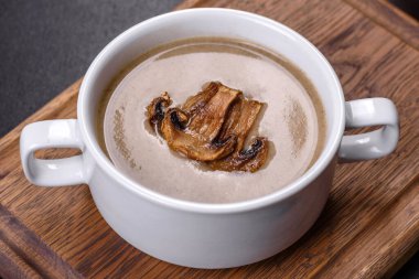 Tahta bir tahtanın üzerinde, üzerinde ekmek kırıntıları, baharatlar ve otlarla birlikte koyu beton bir zemin üzerinde taze, lezzetli bir mantar püresi çorbası. Vejetaryen mutfağı