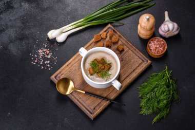 Tahta bir tahtanın üzerinde, üzerinde ekmek kırıntıları, baharatlar ve otlarla birlikte koyu beton bir zemin üzerinde taze, lezzetli bir mantar püresi çorbası. Vejetaryen mutfağı