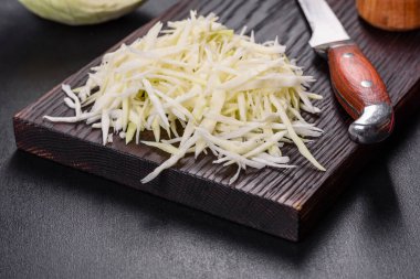 Bir parça lahana kafası ve kesilmiş lahana salatası. Koyu beton arka planda ahşap kesim tahtası.