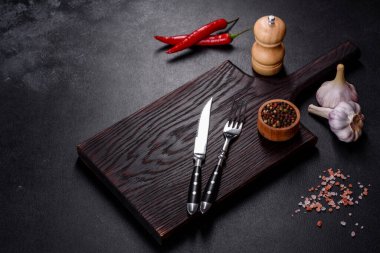 İçinde bıçak, çatal ya da kaşık olan boş bir tabak. Koyu beton arka planda tahta kesim tahtası var. Ev aletleri ve ev yemeği malzemelerinin hazırlanması