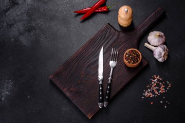 İçinde bıçak, çatal ya da kaşık olan boş bir tabak. Koyu beton arka planda tahta kesim tahtası var. Ev aletleri ve ev yemeği malzemelerinin hazırlanması