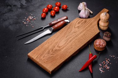 İçinde bıçak, çatal ya da kaşık olan boş bir tabak. Koyu beton arka planda tahta kesim tahtası var. Ev aletleri ve ev yemeği malzemelerinin hazırlanması