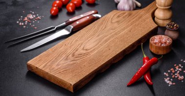 İçinde bıçak, çatal ya da kaşık olan boş bir tabak. Koyu beton arka planda tahta kesim tahtası var. Ev aletleri ve ev yemeği malzemelerinin hazırlanması