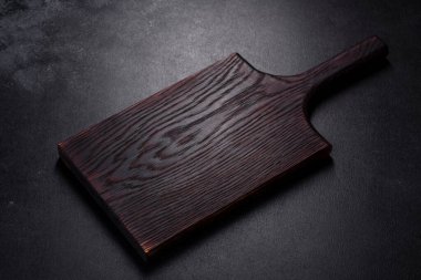 İçinde bıçak, çatal ya da kaşık olan boş bir tabak. Koyu beton arka planda tahta kesim tahtası var. Ev aletleri ve ev yemeği malzemelerinin hazırlanması