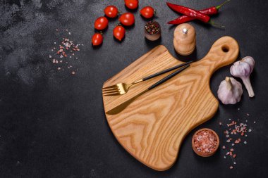 İçinde bıçak, çatal ya da kaşık olan boş bir tabak. Koyu beton arka planda tahta kesim tahtası var. Ev aletleri ve ev yemeği malzemelerinin hazırlanması