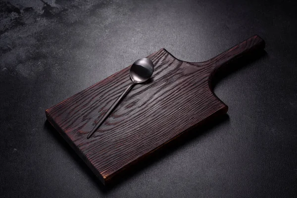 İçinde bıçak, çatal ya da kaşık olan boş bir tabak. Koyu beton arka planda tahta kesim tahtası var. Ev aletleri ve ev yemeği malzemelerinin hazırlanması