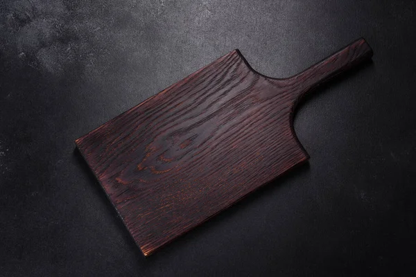 İçinde bıçak, çatal ya da kaşık olan boş bir tabak. Koyu beton arka planda tahta kesim tahtası var. Ev aletleri ve ev yemeği malzemelerinin hazırlanması