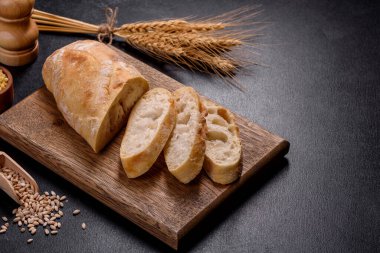 Ahşap bir kesme tahtasının üzerinde koyu beton arka planda dilimlenmiş Fransız ekmeği. Yemek masasını hazırlıyorum.