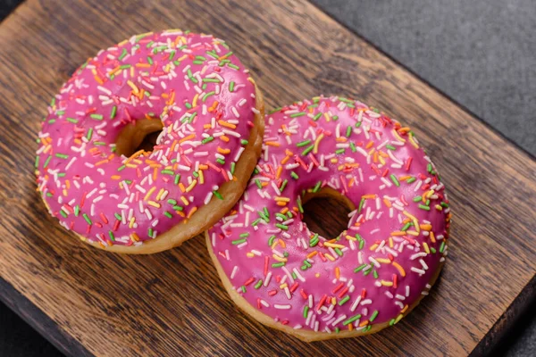 A beautiful doughnut with pink glaze and colored sprinkle on a dark concrete background. Sweets to the dinner table