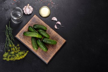 Tahta kesme tahtasındaki sarımsak, tuz, baharat ve otlarla kaplı lezzetli taze salatalıklar koyu beton arka planda. Salatalık koruma hazırlığı