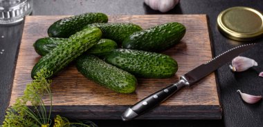 Tahta kesme tahtasındaki sarımsak, tuz, baharat ve otlarla kaplı lezzetli taze salatalıklar koyu beton arka planda. Salatalık koruma hazırlığı