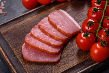 Lezzetli tütsülenmiş et, ahşap bir kesme tahtasının üzerinde koyu gri bir arka planda kesilmiş.