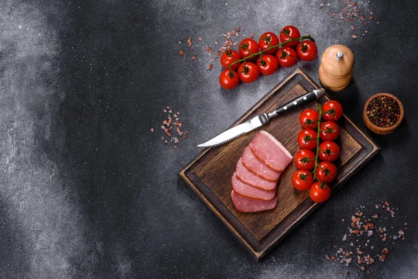 Delicious smoked meat cut with slices on a wooden cutting board against a dark grey concrete background