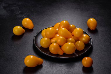 Pear-shaped small yellow tomatoes in a ceramic plate on a dark concrete table. Salad ingredients