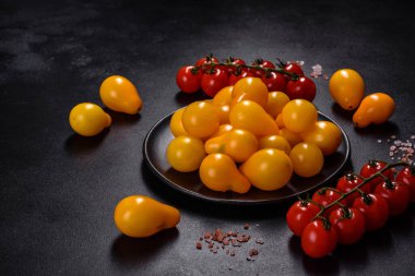 Pear-shaped small yellow tomatoes in a ceramic plate on a dark concrete table. Salad ingredients