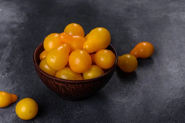 Pear-shaped small yellow tomatoes in a ceramic plate on a dark concrete table. Salad ingredients