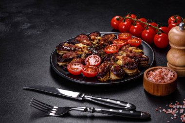 Fresh eggplant baked with minced meat, spices and herbs on a black plate against a dark concrete background