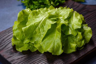 Salad, parsley and dill on a dark cutting board against a blue concrete background. Cooking a vegetarian dish with fresh greens
