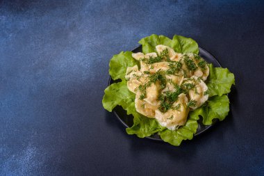Delicious fresh cooked dumplings with potatoes embellished with greens and lettuce leaves on a dark plate against a blue concrete background