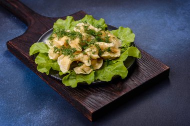 Delicious fresh cooked dumplings with potatoes embellished with greens and lettuce leaves on a dark plate against a blue concrete background
