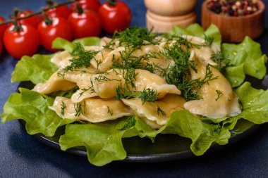 Delicious fresh cooked dumplings with potatoes embellished with greens and lettuce leaves on a dark plate against a blue concrete background