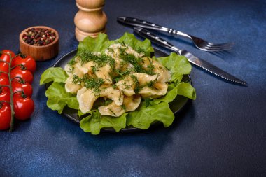 Delicious fresh cooked dumplings with potatoes embellished with greens and lettuce leaves on a dark plate against a blue concrete background