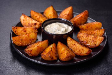 Baked potato wedges with cheese and herbs and tomato sauce on a dark background - homemade organic vegetable vegan vegetarian potato wedges snack food
