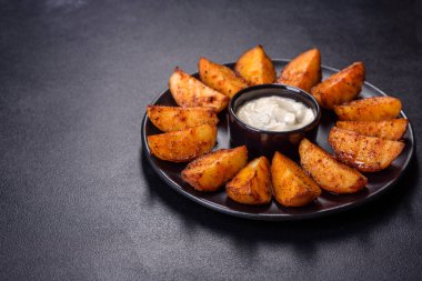 Baked potato wedges with cheese and herbs and tomato sauce on a dark background - homemade organic vegetable vegan vegetarian potato wedges snack food