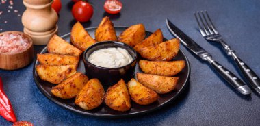 Baked potato wedges with cheese and herbs and tomato sauce on a dark background - homemade organic vegetable vegan vegetarian potato wedges snack food