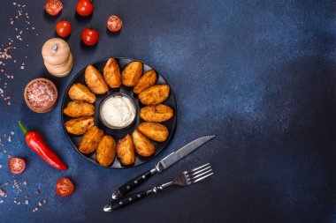 Baked potato wedges with cheese and herbs and tomato sauce on a dark background - homemade organic vegetable vegan vegetarian potato wedges snack food
