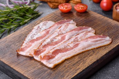 Raw smoked bacon on a wooden board with several cut pieces