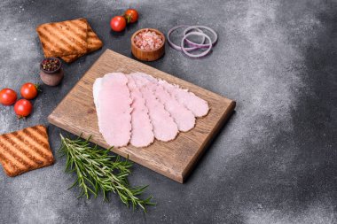 Sliced prosciutto ham on wooden cutting board. Black concrete background