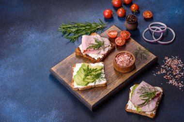 Fresh, delicious ham, butter, avocado and sesame seeds sandwiches on a wooden cutting board. Delicious healthy food