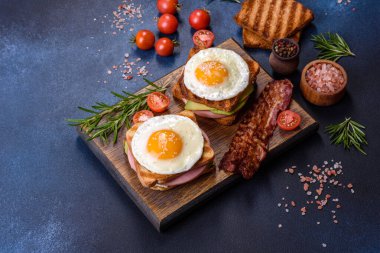 Fresh, delicious sandwiches with fried egg, ham, butter, avocado and sesame seeds on a wooden cutting board. Delicious healthy food