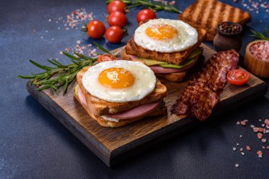 Fresh, delicious sandwiches with fried egg, ham, butter, avocado and sesame seeds on a wooden cutting board. Delicious healthy food