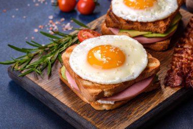 Fresh, delicious sandwiches with fried egg, ham, butter, avocado and sesame seeds on a wooden cutting board. Delicious healthy food