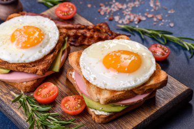 Fresh, delicious sandwiches with fried egg, ham, butter, avocado and sesame seeds on a wooden cutting board. Delicious healthy food