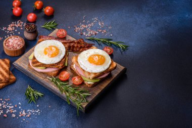 Fresh, delicious sandwiches with fried egg, ham, butter, avocado and sesame seeds on a wooden cutting board. Delicious healthy food