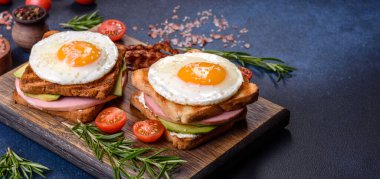 Fresh, delicious sandwiches with fried egg, ham, butter, avocado and sesame seeds on a wooden cutting board. Delicious healthy food