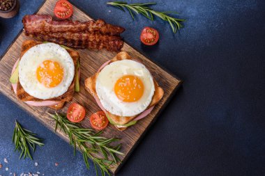 Fresh, delicious sandwiches with fried egg, ham, butter, avocado and sesame seeds on a wooden cutting board. Delicious healthy food