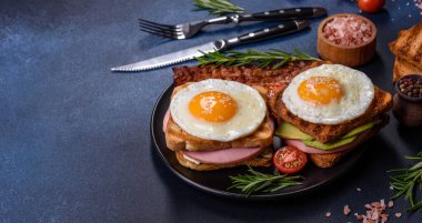 Fresh, delicious sandwiches with fried egg, ham, butter, avocado and sesame seeds on a wooden cutting board. Delicious healthy food