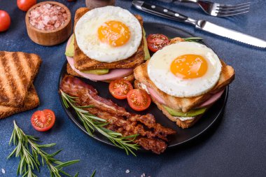 Fresh, delicious sandwiches with fried egg, ham, butter, avocado and sesame seeds on a wooden cutting board. Delicious healthy food