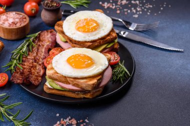 Fresh, delicious sandwiches with fried egg, ham, butter, avocado and sesame seeds on a wooden cutting board. Delicious healthy food