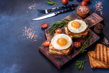 Fresh, delicious sandwiches with fried egg, ham, butter, avocado and sesame seeds on a wooden cutting board. Delicious healthy food