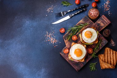 Fresh, delicious sandwiches with fried egg, ham, butter, avocado and sesame seeds on a wooden cutting board. Delicious healthy food