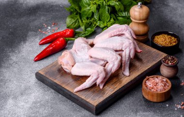 Raw chicken wings with ingredients for cooking on a wooden cutting board over gray slate