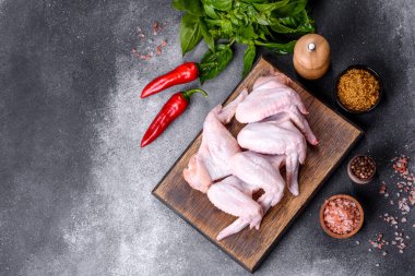 Raw chicken wings with ingredients for cooking on a wooden cutting board over gray slate