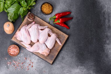 Raw chicken wings with ingredients for cooking on a wooden cutting board over gray slate