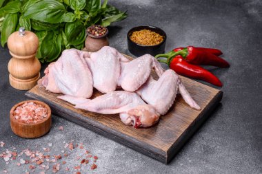 Raw chicken wings with ingredients for cooking on a wooden cutting board over gray slate