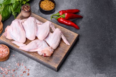 Raw chicken wings with ingredients for cooking on a wooden cutting board over gray slate
